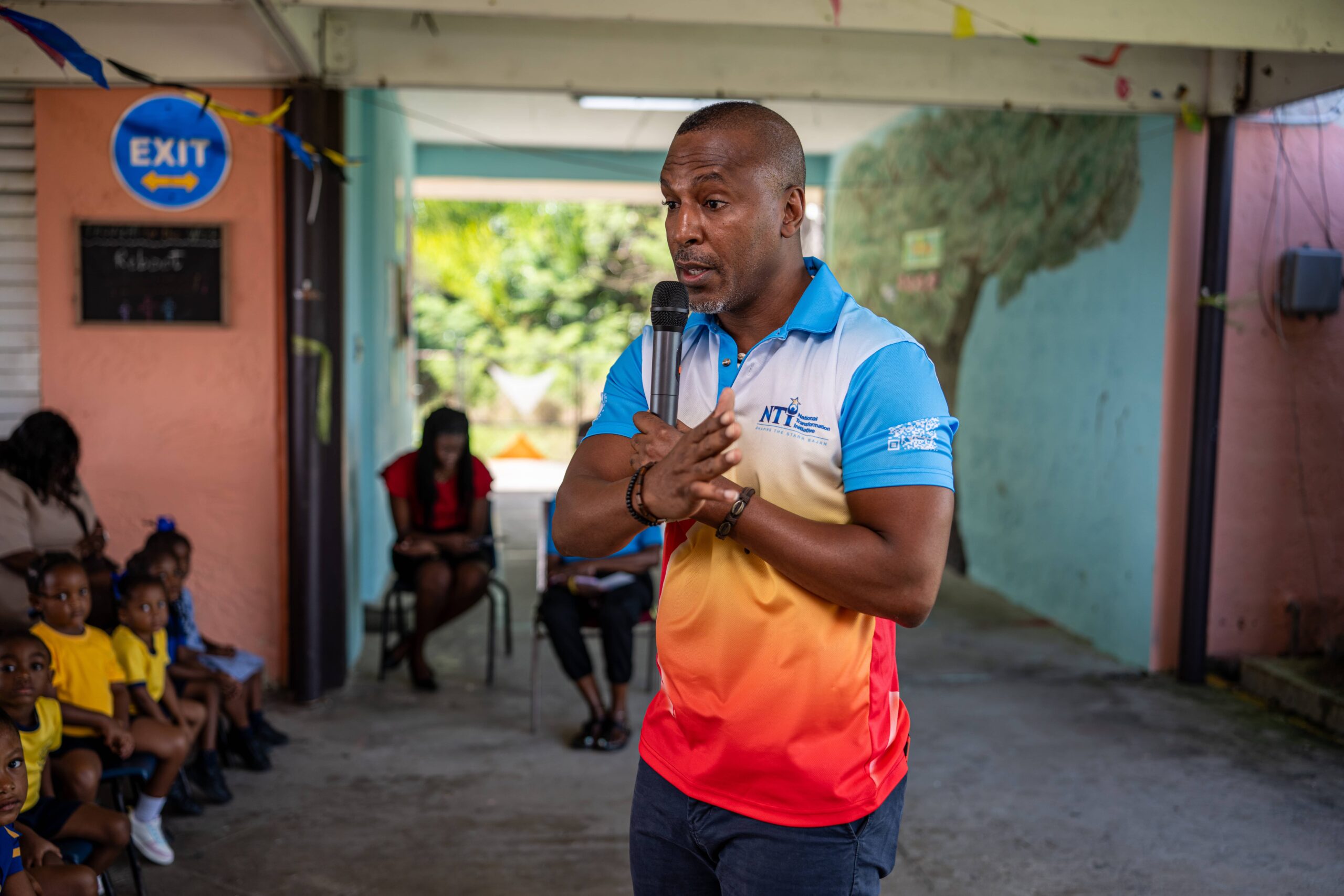 Man giving a talk with a microphone while young children sit and listen
