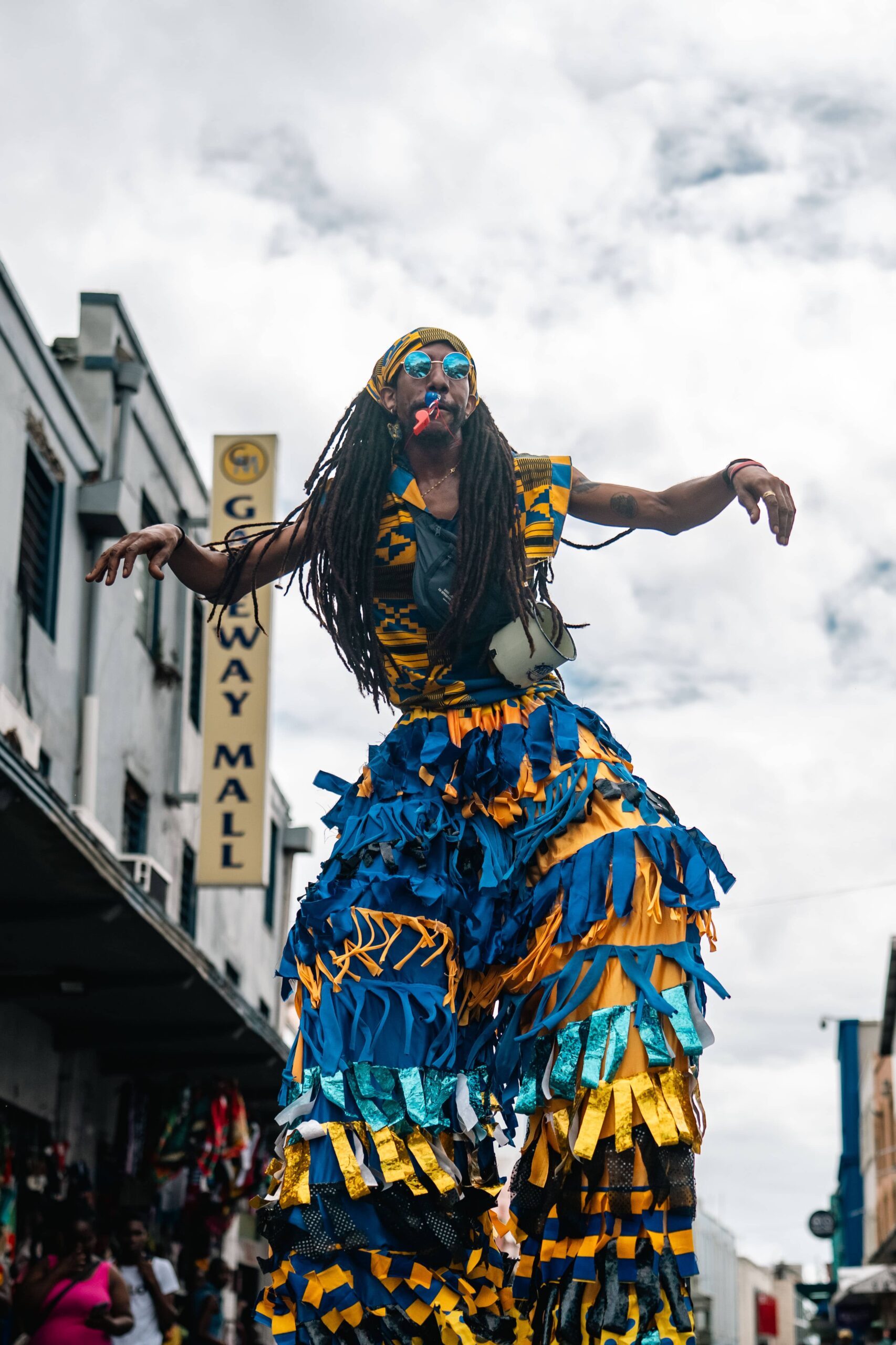 Performer on stilts wearing a blue and yellow ruffled costume in a city street