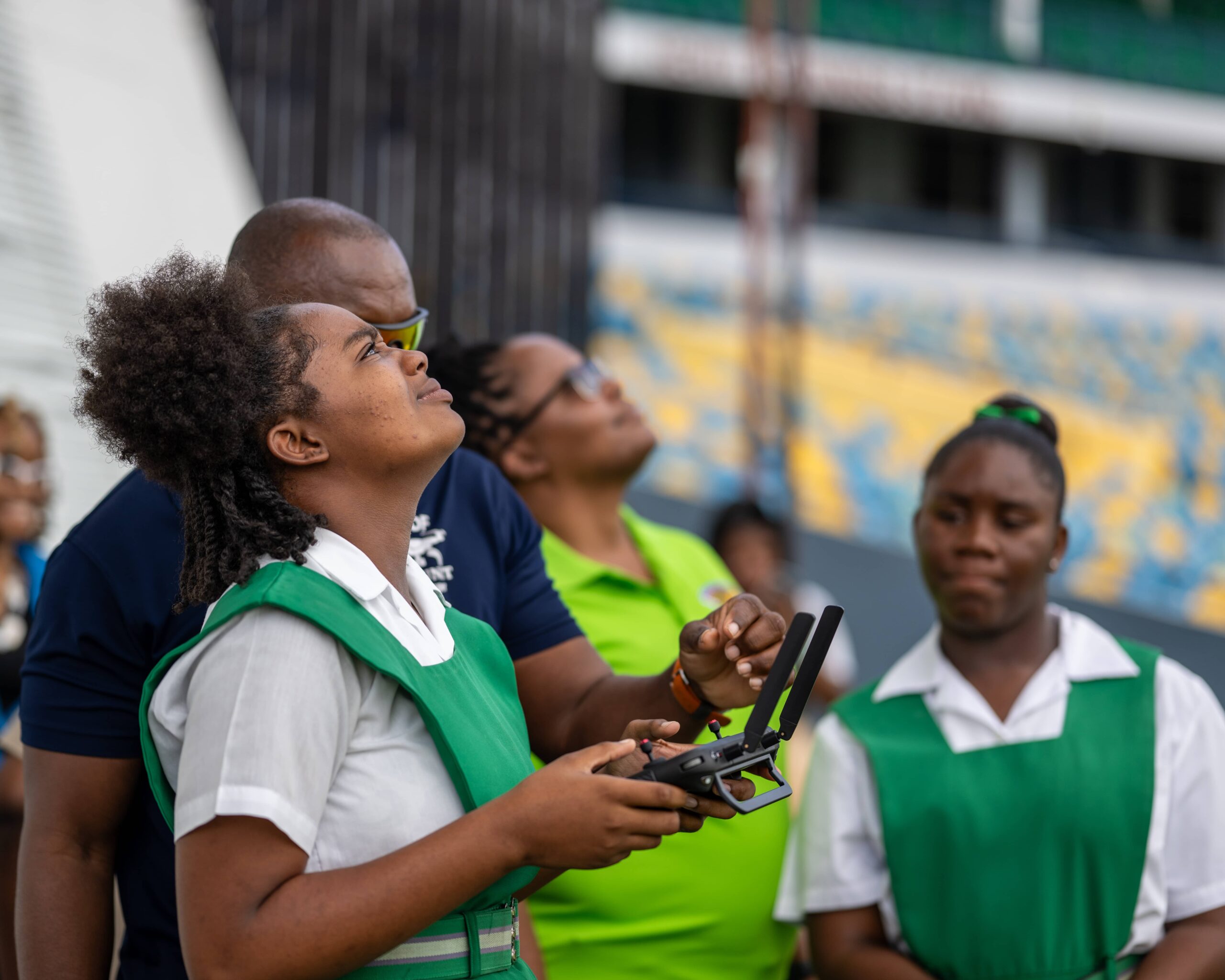 Student in a green uniform holding a drone controller while others watch